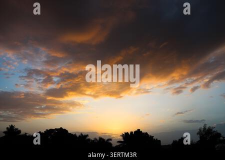 Dramatic cloudscape during sunset with glowing horizon light. Nature landscape capturing an intense sunset with richly detailed clouds. Stock Photo