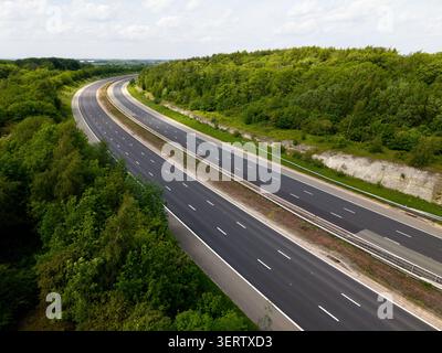 Aerial landscape view above a deserted three lane motorway in the UK cutting through woodland countryside with hard shoulder and copy space Stock Photo