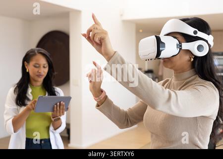 Diverse female coworkers demonstrating virtual reality at home with white headset and tablet Stock Photo