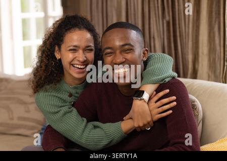Couple hugging and smiling while sitting on beige sofa by white-paned window with sweaters Stock Photo