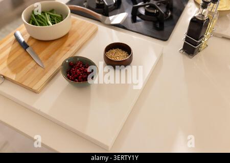 Wooden board, blue knife, green beans, pomegranate and pine nuts sitting near gas stove on counter Stock Photo