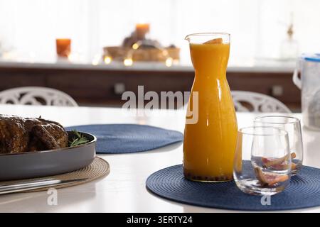 Carafe of orange juice and two glasses are sitting on dining table near glazed roast Stock Photo