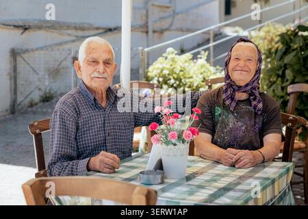 June 25, 2022, village of Plati, Crete, Greece: Happy elderly couple sitting at the table of their restaurant in a small Cretan village Stock Photo