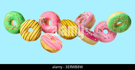 Yummy donuts covered with icing falling on light blue background Stock Photo