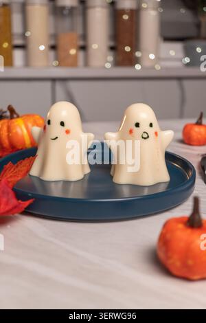 Cute ghost-shaped marshmallow desserts on blue plate with mini pumpkins Stock Photo