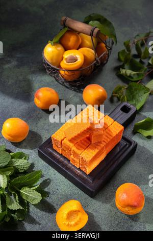Apricot fruit paste bars displaying a healthy sweet snack option, arranged with fresh apricots in a basket, loose fruits, and green mint leaves on a d Stock Photo