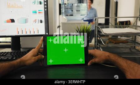 POV of manager uses tablet with green screen template, looking at chroma key layout and sitting in coworking space. Stock Photo