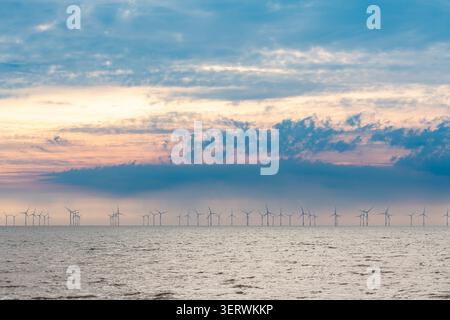 Offshore wind farm stretching across the horizon at sunset over a calm sea under a pastel sky Stock Photo