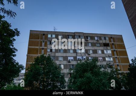 It’s a typical Communist-era apartment block, those big concrete buildings with rows of windows and balconies. Looks like it’s in a residential area w Stock Photo