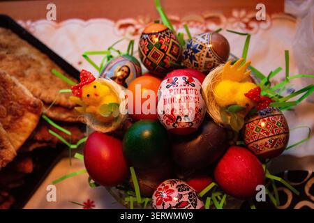 This is a festive Easter display featuring a collection of vibrantly decorated eggs nestled in green grass-like material. Among them are two small, ye Stock Photo