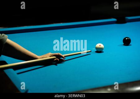 A person is playing pool, aiming at the white ball with a cue stick on a blue table. Stock Photo