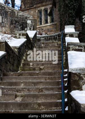 A stone staircase with snow on the steps and railings, leading up to a building with large windows. Stock Photo