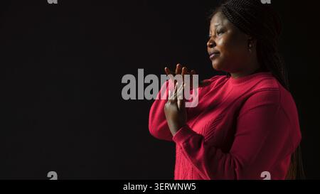 Side-view portrait of female model performing timeout, pause motion on camera, with African American woman in Black background displaying a t shape stop symbol with her arms, indicating no. Stock Photo