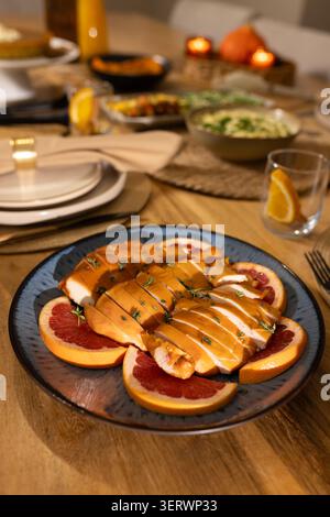 Glazed sliced poultry is resting on plate over citrus wedges on wooden table, sauce and herbs Stock Photo