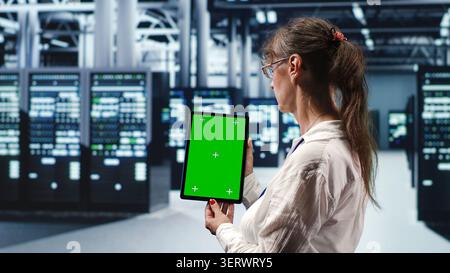 Senior expert in servers facility housing high-end processors capable of quickly and efficiently performing complex computations and data analysis, using mockup tablet to service hardware. Stock Photo