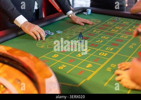 Hands reach for chips on a green roulette table. Children and adults place bets, engaged in a lively game. The atmosphere is vibrant and competitive. Stock Photo