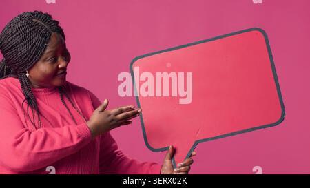 African American beauty holding a red speech bubble mockup for text messages and notes in her right hand, black lady nodding in agreement with the content of the word-bubble copyspace template. Stock Photo