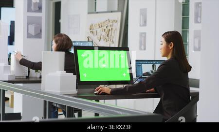 Architect using computer with green screen at workstation in agency office, looking at blank mockup template on monitor, engineer employed at a real estate small business, tripod shot. Stock Photo