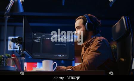 Cheerful programmer listening music while doing web development during remote job shift in neon lit home office, finishing coding project, iT expert enjoying audio podcast, working on PC. Stock Photo