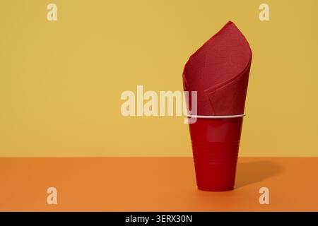 Red plastic cup with blue and red straws and napkin on orange table with yellow background Stock Photo