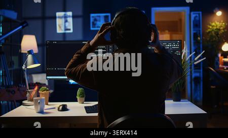 Technician putting headphones on while using coding to fortify firewalls, teleworking for IT company, computer scientist listening music and upgrading binary code scripts in home office. Stock Photo