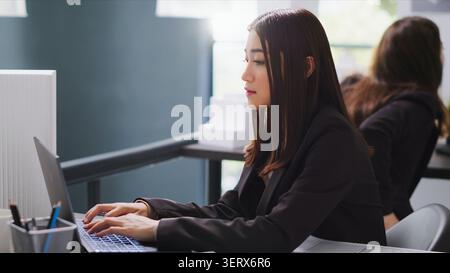 Asian architect translating floor plan measurements on laptop, studying architectural blueprints and helping contractors with dimensions, Real estate agency worker overseeing project, Handheld shot. Stock Photo