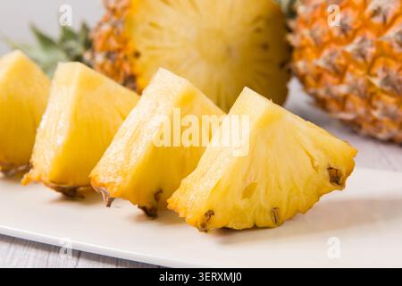 Pineapple slices are arranged on a white plate with whole and half pineapples in the background Stock Photo