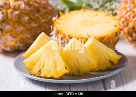 Pineapple slices are arranged on a white plate with whole and half pineapples in the background Stock Photo