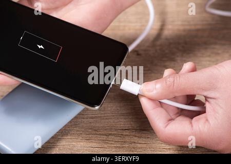 Hand plugging usb cable into smartphone, charging low battery from power bank Stock Photo