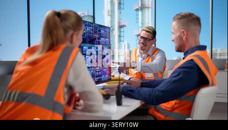 Engineers Working Together, Monitoring Electronic Controls At Busy Industrial Plant. Stock Photo