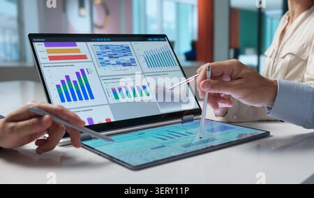 Financial Analysts Collaborate As They Examine Digital KPI Dashboards On Tablets. Stock Photo