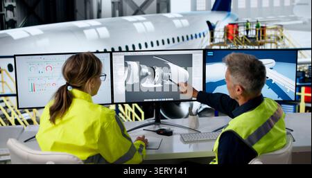 Two Engineers Examine Airplane Engine Parts On Screen To Improve Safety. Stock Photo