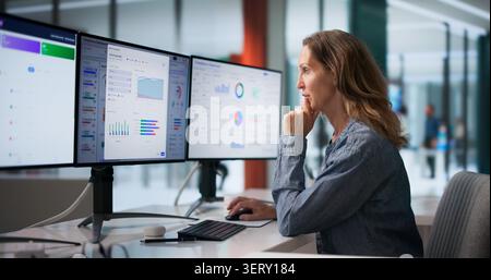 Woman Reviews Multiple Screens Displaying Compliance Data And Regulatory Reports. Stock Photo