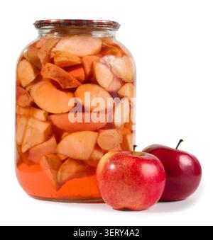 Canned apples in a glass jar on a white background. Fresh apples are in the foreground. Stock Photo