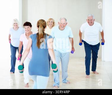 Dumbbells, class and woman with senior people for exercise, wellness and stretching for mobility. Retirement, gym and trainer with elderly group with Stock Photo