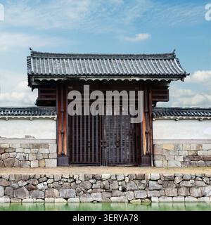 Traditional Japanese Castle Gate with Tiled Roof and Stone Wall Reflected in Moat Stock Photo
