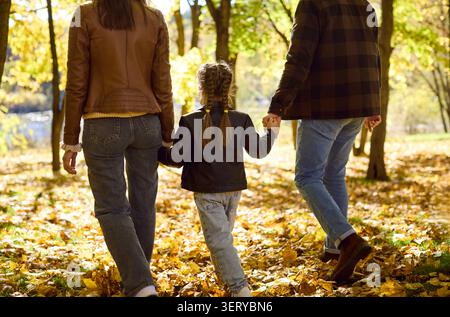 Parents holding daughters hands on autumn walk, family back view in park Stock Photo
