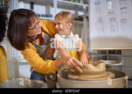 smiling artists having fun while shaping a clay pot on a wheel at pottery workshop.  Creative, hobby ,workshop  concept Stock Photo