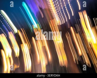 Blurred city lights streaks at night, capturing neon trails and bokeh from moving traffic, energetic vertical motion with warm and cool color Stock Photo