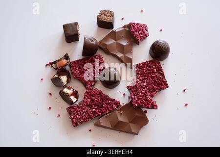 Assorted broken chocolate with raspberries and chocolate candies with fillings on a white background Stock Photo