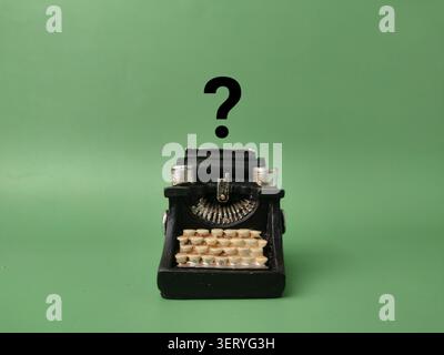 A small black vintage typewriter model sits centered on a solid green background beneath an overlaid black question mark. Stock Photo