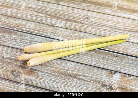 Vibrant green and pale yellow lemongrass stalks arranged diagonally on textured light brown wood. Culinary herb, ingredient for Asian cuisine, healthy Stock Photo