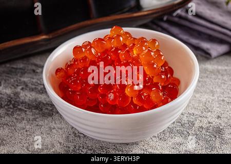 Closeup of fresh red salmon roe glistening in ceramic bowl with soft lighting highlighting translucent texture and vibrant color for gourmet food pres Stock Photo