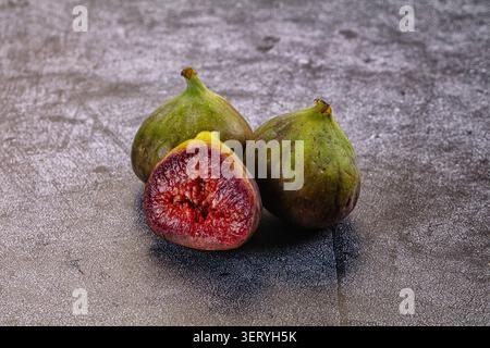 Three fresh green figs on a textured gray surface, one cut in half to show vibrant red interior, natural lighting, healthy eating, organic fruit, clos Stock Photo