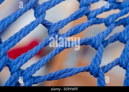 Close-up view of a blue rope net with thick twisted cords and knotted intersections, forming a diagonal woven pattern against a softly blurred background Stock Photo