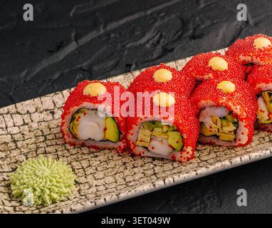 Bright red California rolls filled with prawns and avocado. Japanese seafood dish topped with spicy mayonnaise drops. Stock Photo