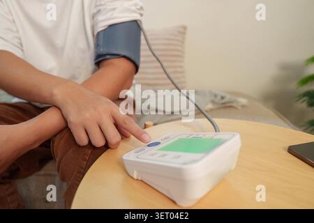A cropped view of a man's arm with a blood pressure cuff, pressing a button on a home monitor for health self-care. - Photomontage Stock Photo