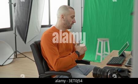 Man photographer pointing at tablet and gesturing with hands at desk in studio, green screen and camera visible; concentration creativity. Stock Photo