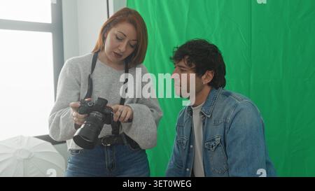 Woman photographer holds camera and shows image to seated man model with hand on shoulder in studio; friendly collaboration. Stock Photo