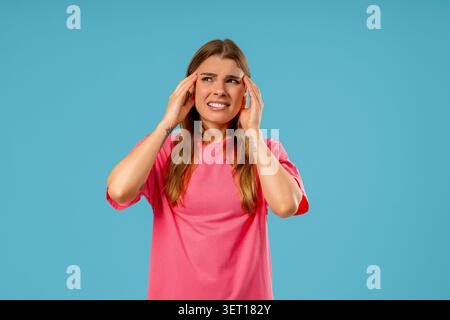 Woman touching massaging temples, suffering from headache, blood pressure on blue studio. Pain, migraine symptoms, illness Stock Photo
